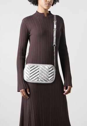 Sac bandoulière argenté métallisé avec un motif matelassé en chevrons, forme rectangulaire et une bandoulière chaîne, assorti à une robe marron côtelée.