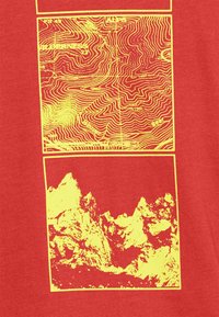 Prenda roja con dos estampados gráficos amarillos: en la parte superior se muestran líneas de contorno, en la parte inferior picos montañosos irregulares. Textura suave.