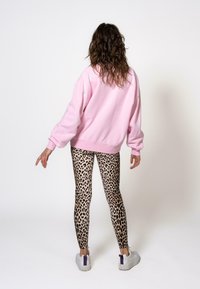Rosa übergroßer Sweater, Leggings mit Leopardenmuster und weiße Sneakers mit lila Akzenten. Glatter Stoff, lässige Passform und kontrastierende Muster.