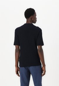 Marinblå kortärmad stickad tröja med en strukturerad kabelmönster och ribbad fåll. Har en klassisk krage och en figursydd silhuett.