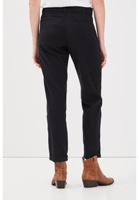 Svarta skräddarsydda byxor med uppvikta avslut, gjorda av ett mjukt tyg. Bärs med bruna ankelkängor med låg klack.