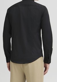 Zwarte langemouwen shirt van gladde stof, met knopen op de manchetten, een afgeronde onderrand en een klassieke kraag. Eenvoudig ontwerp zonder patronen.