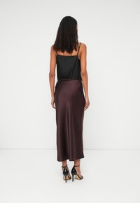 Fekete selyem camisole egy bordó selyem midi szoknyával, sima textúrával és karcsú fazonnal, fekete magassarkú cipőkkel viselve.