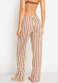 Ριγέ παντελόνια με άνετη εφαρμογή, με κάθετες καφέ και κρεμ ρίγες. Κατασκευασμένα από μαλακό υλικό με ελαστική μέση.