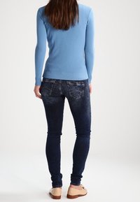 Ljusblå långärmad topp kombinerad med mörkblå smala jeans. Outfiten har en åtsittande design och ribbat stickat detaljer vid ärmsluten.