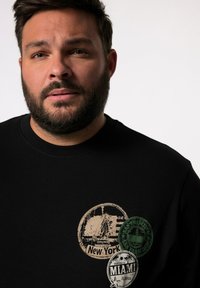 Schwarzer Sweatshirt mit runden Grafik-Patches, die "New York", "Miami" und "San Francisco" in Beige und Grün zeigen. Weicher Stoff, Rundhalsausschnitt.