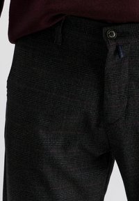 Geruite zwarte broek met een subtiele ruitpatroon, gemaakt van textuurstof, met een knoopsluiting en riemlussen.