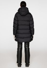 Svart puffjacka med huva, med horisontell sömnad och medellång design. Kombinerad med svarta läderbyxor och stabila svarta kängor.