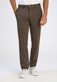 Bruine op maat gemaakte broek van soepel materiaal met een slim fit, voorzien van zijzakken, een knoopsluiting en gecombineerd met witte sneakers.