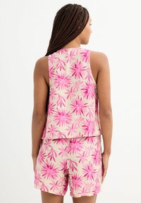 Conjunto de top sin mangas y pantalones cortos con estampado floral que presenta una base cremosa con flores de color rosa brillante. Tejido suave, ajuste holgado y diseño sin costuras.