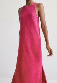 Robe en maille rose sans manches avec une silhouette droite, des fentes latérales et une finition texturée, adaptée pour une tenue décontractée ou par temps chaud.