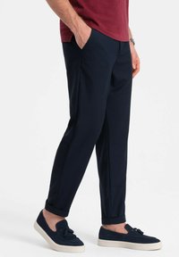 Pantaloni tapered blu navy con una texture liscia e tasche laterali, abbinati a scarpe slip-on blu scuro con un dettaglio a nappina.