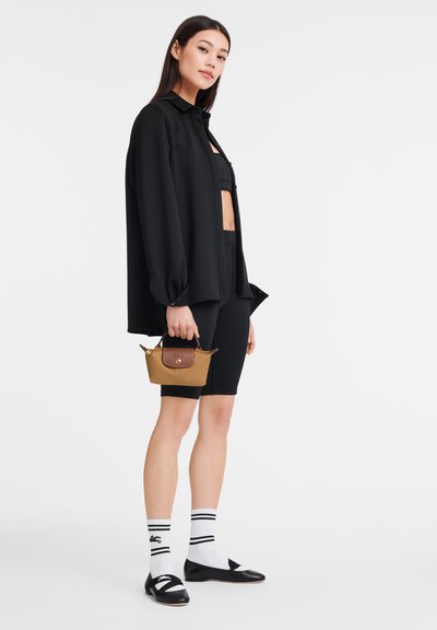 Schwarzes Oversized-Shirt, schwarzes kurzes Top, schwarze Radlerhosen, weiße Socken mit Streifen, schwarze Ballerinas und eine kleine braune Handtasche mit Ledeerakzenten.