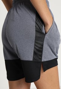 Šedé sportovní šortky s texturovanou látkou, s černými bočními panely, elastickým pasem a šikmými kapsami přes boky.