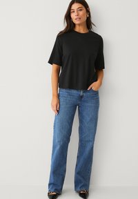 Schwarzes kurzes Oberteil mit Rundhalsausschnitt, kombiniert mit hellblauen weit geschnittenen Jeans. Das Outfit wird durch schwarze High Heels ergänzt.