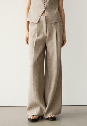 Pantaloni beige in lino a gamba larga con pince frontali, indossati con un gilet senza maniche abbottonato abbinato e sandali con plateau neri.