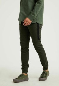 Olijfgroene broek met zwarte accenten aan de zijkanten, slim fit, casual stijl. Gecombineerd met groene veterschoenen met een gestructureerde grijze zool.