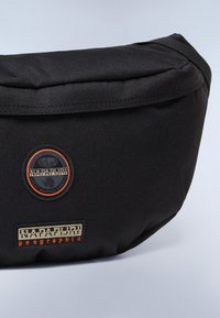 Borsa in tessuto nera a vita con forma arrotondata. Presenta un logo circolare e una patch rettangolare con del testo. Superficie testurizzata e spallacci robusti.