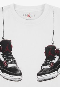 Λευκό βαμβακερό T-shirt με γραφικό που απεικονίζει μαύρα και κόκκινα αθλητικά παπούτσια με λευκές λεπτομέρειες, λεπτομερή ραφές και κορδόνια, κρεμασμένα από γραμμές.