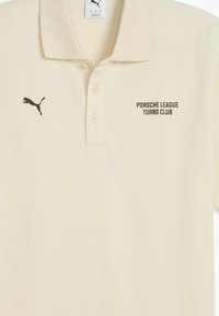 Polo beige avec un logo noir de Puma à gauche et le texte "Porsche League Turbo Club" sur le côté droit.