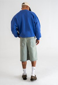 Hanorac oversized albastru, şorturi din denim bleu deschis, şosete albe, pantofi maro. Design simplu, croi lejer. Cusături notabile pe şorturi.