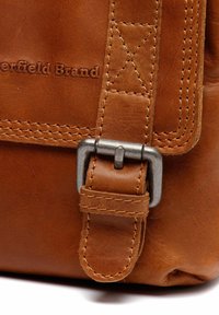 Borsa in pelle marrone con una fibbia metallica visibile e dettagli di cucitura. La texture è liscia, con marchio in rilievo sulla superficie.