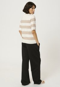 Lahka pletena majica z vodoravnimi bež in belimi črtami, kratkimi rokavi, kombinirana z ohlapnimi črnimi hlačami. Minimalističen dizajn, brez vidnih logotipov.