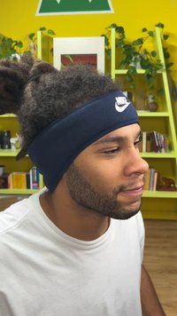 Tamsiai mėlynas „Nike“ galvos juostos dėvimas žmogaus su tamsiais garbanotais plaukais. Artimas vaizdas, pabrėžiantis sklandžią medžiagą ir logotipo detalę priekyje.