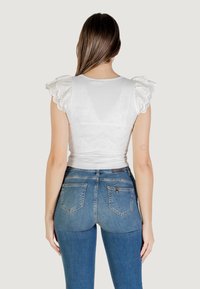Top in cotone bianco con maniche a volant in pizzo occhiellato, abbinato a jeans skinny in denim blu con tasche posteriori e vita aderente.