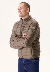 Giacca imbottita verde oliva con design a canale trapuntato, colletto alto e tasche laterali. Presenta una toppa con logo sulla manica sinistra.
