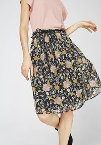 Bloemenrok van zwarte stof met een doorschijnende overlay, versierd met kleurrijke bloemen. Verstelbare tailleband met zwarte strikdetails. Tot de knie.