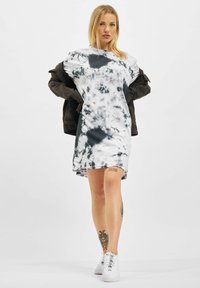Kortärmad, tie-dye klänning i svart och vitt, med en avslappnad passform och rund halsringning, kombinerad med en mörk denimjacka och vita sneakers.