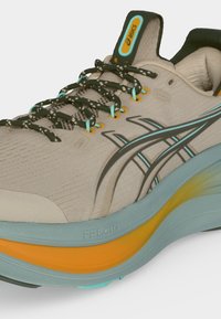 Μπεζ αθλητικό παπούτσι Asics με μαύρο και μπλε λογότυπο, μαύρα και λευκά κορδόνια με σχέδιο και μπλε-πορτοκαλί απορροφητική σόλα.