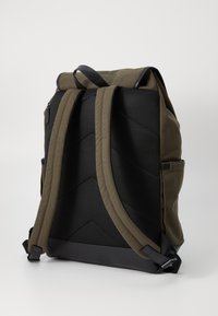 Sac à dos en tissu olive vert avec un dos en maille noire texturée et des bretelles rembourrées et réglables. Il dispose d'un dessus plat et d'une poche latérale.