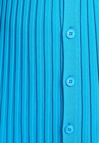 Blue pleated fabric with a vertical texture. Features matching blue buttons along the front, enhancing the overall uniformity of the design.