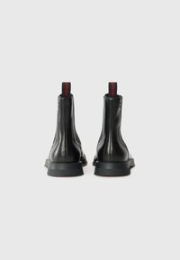 Black leather ankle boots with a smooth texture, rounded toe, and contrasting red logo details on the heel. Low rubber outsole.