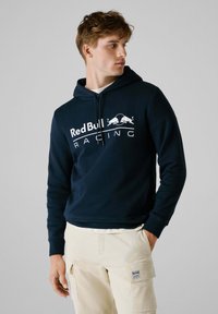 Marineblauwe hoodie met capuchon, voorzien van een wit "Red Bull Racing" logo en een afbeelding van twee stieren op de borst. Zachte stof, klassieke pasvorm.