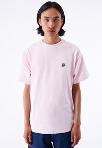 Camiseta de algod�ón de color rosa claro con cuello redondo y mangas cortas. Presenta un pequeño logo bordado en negro en el lado izquierdo del pecho.