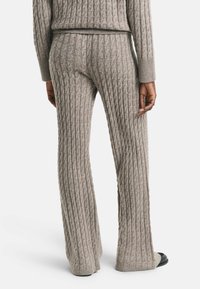 Grijze gebreide broek met een ribbelstructuur, met een flared design en contrasterende boorden. De stof lijkt zacht en comfortabel.