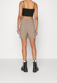 Shorts rayés marron et beige à taille haute, avec deux poches arrière. Associés à des bottines noires à lacets.