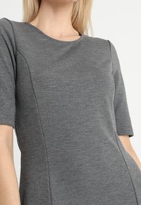 Haut à manches courtes gris en matériau doux et extensible. Il présente un col rond et des épaules sans coutures pour une coupe ajustée.