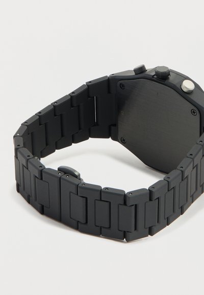 Μαύρο μεταλλικό μπρασελέ ρολογιού με μεγάλα συνδέσμους και ορθογώνιο, κουμπωμένο καντράν, εμφανιζόμενο από πίσω σε λευκό φόντο.