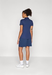 Camisa polo azul-escuro de mangas curtas, combinada com uma saia-short correspondente. Apresenta um colarinho e um logotipo discreto nas costas.