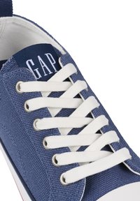 Blauwe canvas sneaker met witte veters, met een gestructureerd oppervlak, ronde neus en een marineblauw label met "GAP" op de tong.