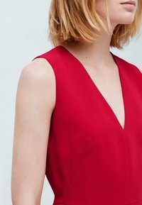 Robe sans manches rouge avec un décolleté en V profond. Tissu lisse avec un design ajusté, comportant des coutures minimales et sans embellissements visibles.