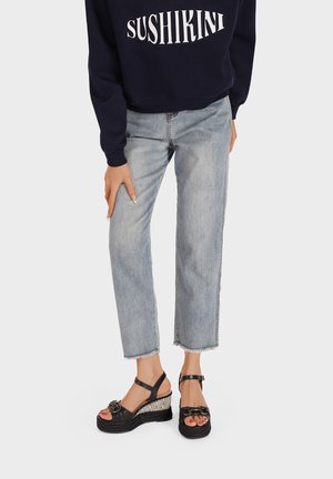 Sandali wedge neri con tacco intrecciato, dotati di una cinghia alla caviglia regolabile e una fibbia decorativa in metallo. Indossati con jeans chiari strappati.