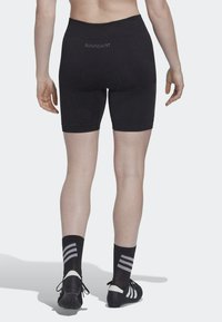 Shorts de sport noirs avec une taille haute, présentant une coupe ajustée et une zone rembourrée. Accompagnés de chaussettes rayées noires et blanches et de chaussures.