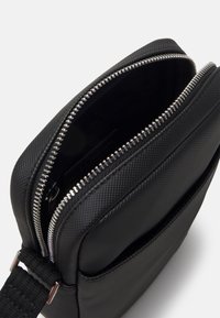 Borsa in nylon nero texturizzato con zip argentata, con apertura superiore e tasca frontale aggiuntiva; tracolla regolabile inclusa.