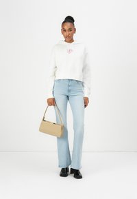 Haut à capuche blanc court avec un logo cœur rose, jean évasé bleu clair et sac à main beige. Des bottines noires à la cheville complètent la tenue.