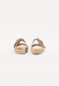 Des sandales en suède beige présentent un design tressé, un dos ouvert et une plateforme basse. Les lanières sont ornées d'une boucle en argent.